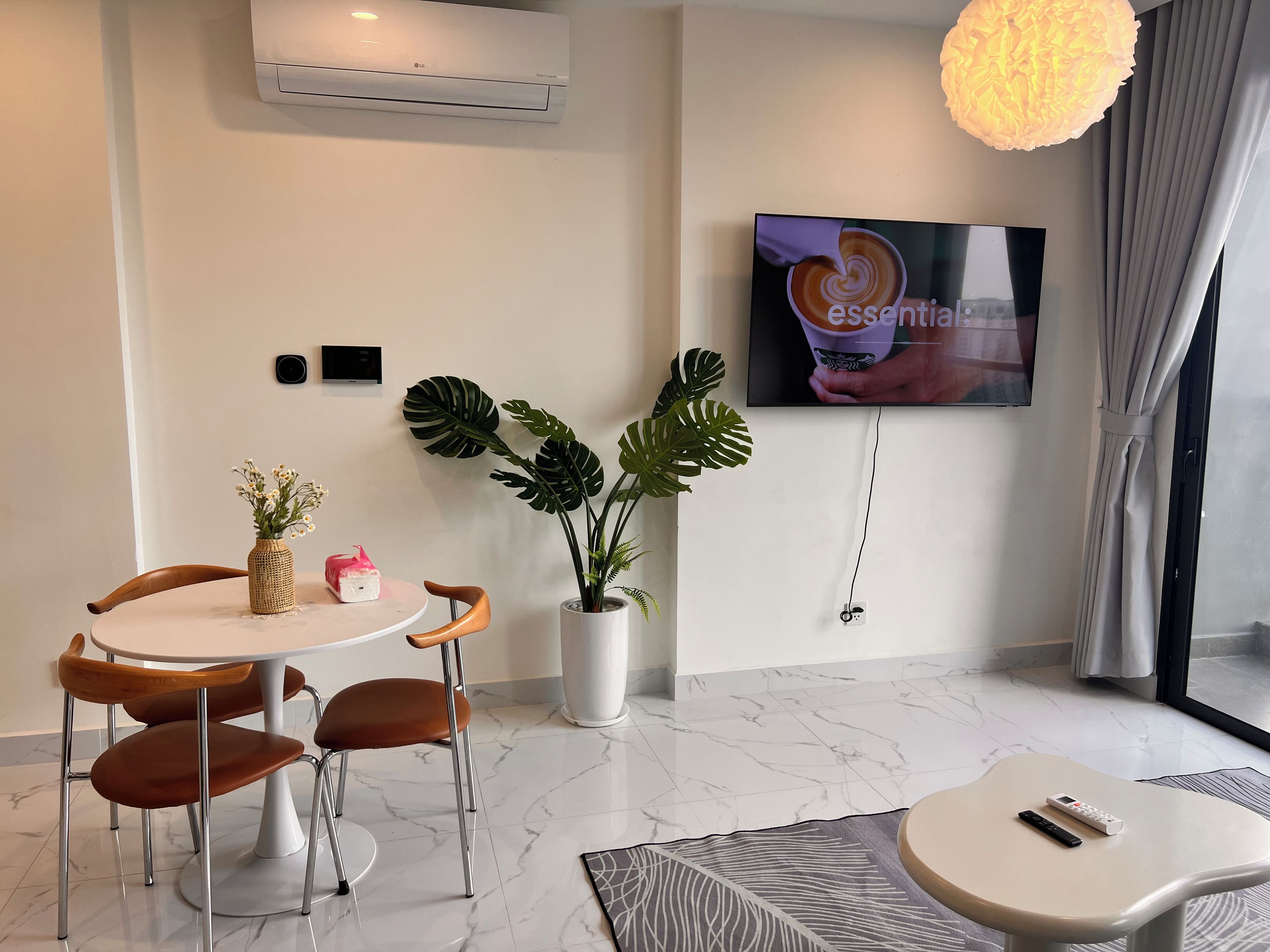 A modern room with a dining table, chairs, a potted plant, a TV, and a remote control on a small table.