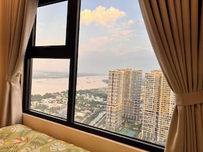 A room with a large window, curtains, and a bed with a patterned bedspread.