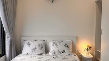 A bedroom with a bed, two pillows, a bedside table with a lamp, and a wall-mounted plant.