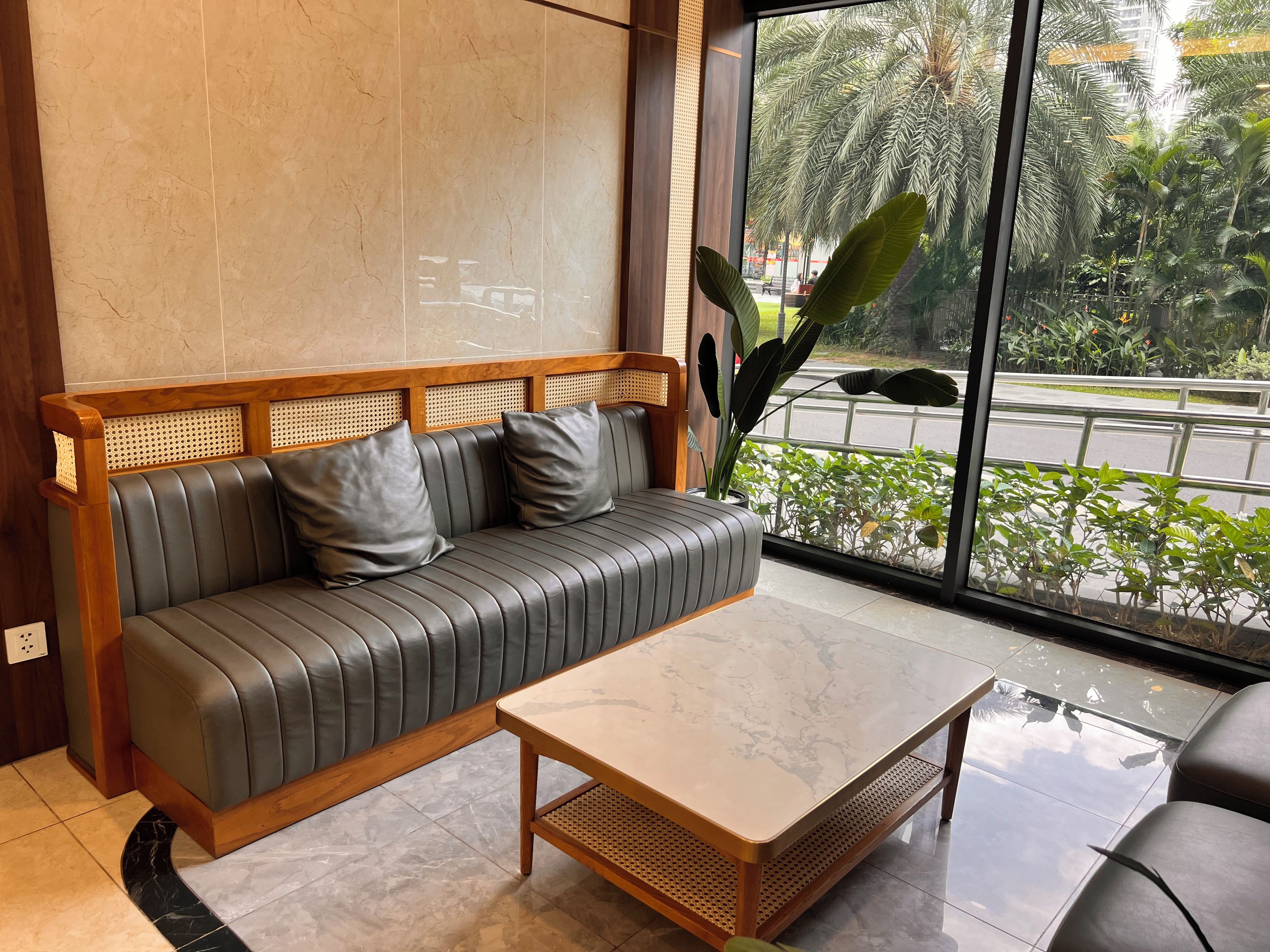 Ein modernes Interieur mit einem Ledersofa, einem Holztisch und einem großen Fenster mit Blick auf Grünflächen und eine Straße.