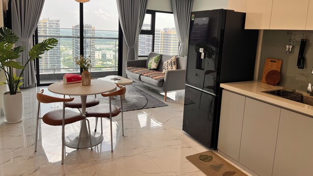 A modern living room with a sofa, dining table, and chairs, a kitchen with a refrigerator, and a large window with a city view.