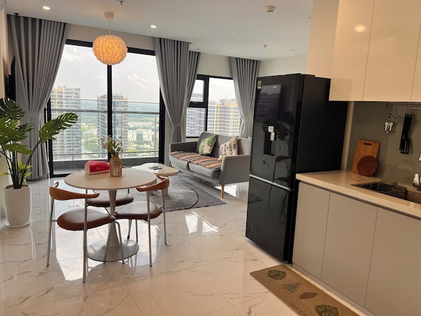 A modern living room with a sofa, dining table, and chairs, a kitchen with a refrigerator, and a large window with a city view.