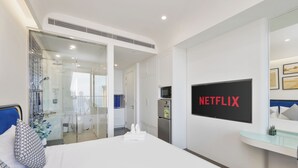 Habitación de hotel con cama, televisor montado en la pared, minibar y vista al baño.