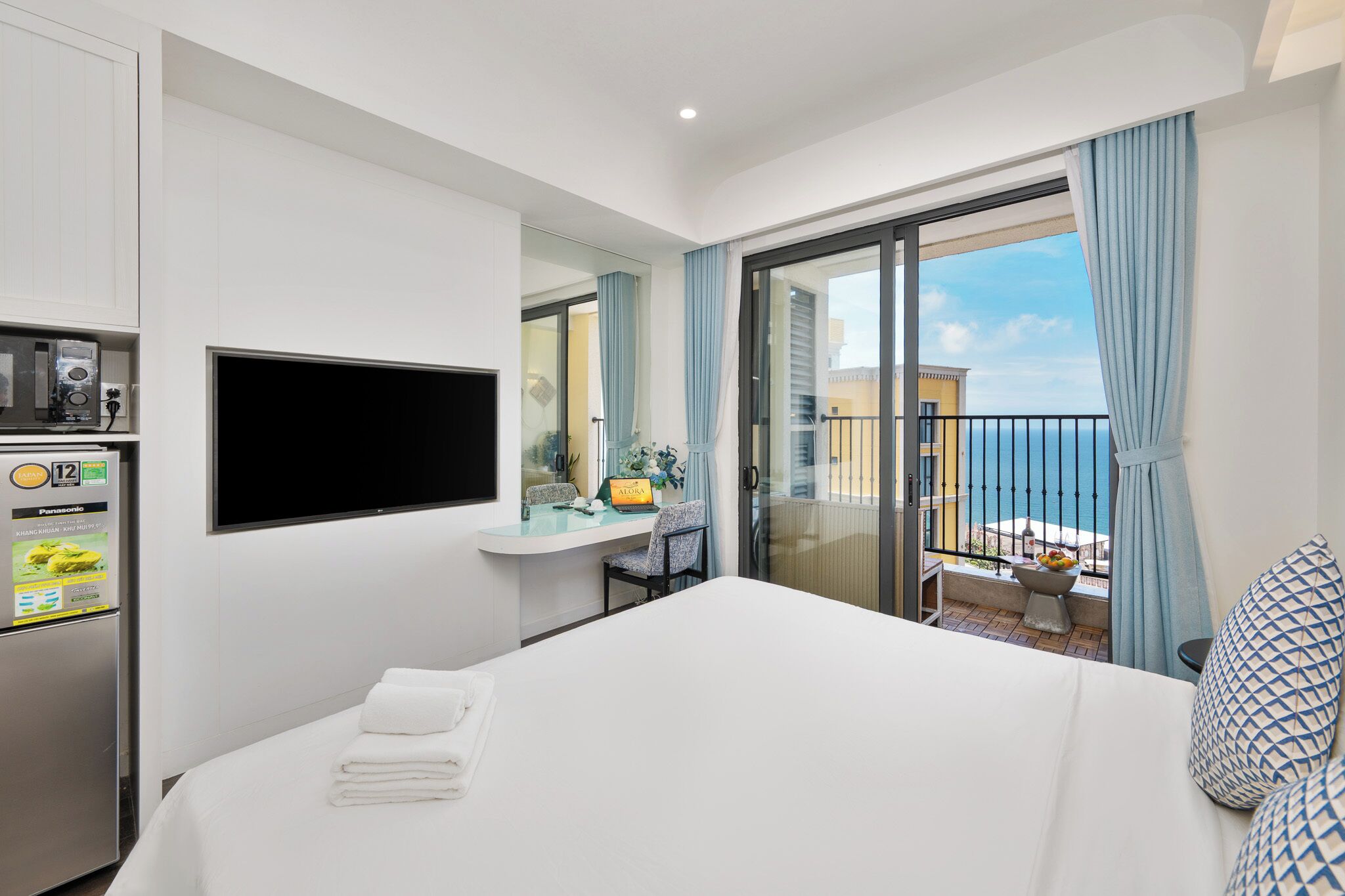 A hotel room with a bed, a TV, a minibar, a desk with a chair, and a balcony with a view.