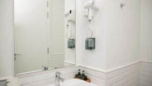 Un baño con un lavabo blanco, un espejo y dos secadores de pelo fijados en la pared.