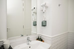 A bathroom with a white sink, a mirror, and two hair dryers mounted on the wall.