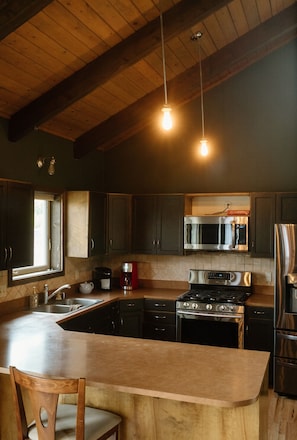A kitchen with a wooden ceiling, a stainless steel refrigerator, a microwave, a stove, and a coffee maker. - Northwood Lodge: 4BR, Sleeps 10, 1 Mile to U of I (Moscow)