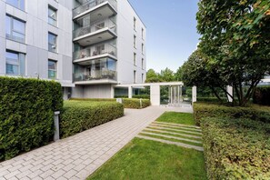 A modern building with a paved walkway, neatly trimmed hedges, and a clear sky. - Baltic Sea Coastal Apartment (Gdańsk)