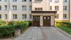 Un edificio residencial de varios pisos con una entrada central, un número de puerta visible y un camino pavimentado que conduce a la entrada.