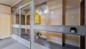 Un pasillo de hotel con puertas de vidrio, un detector de incendios, un ascensor amarillo y una planta en maceta.
