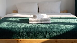 A bed with a green bedspread and two rolled towels stacked on top. - Woronicza Urban Studio #1 (Kraków)