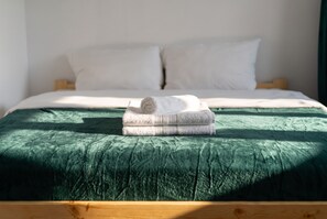 A bed with a green bedspread and two rolled towels stacked on top. - Woronicza Urban Studio #1 (Kraków)