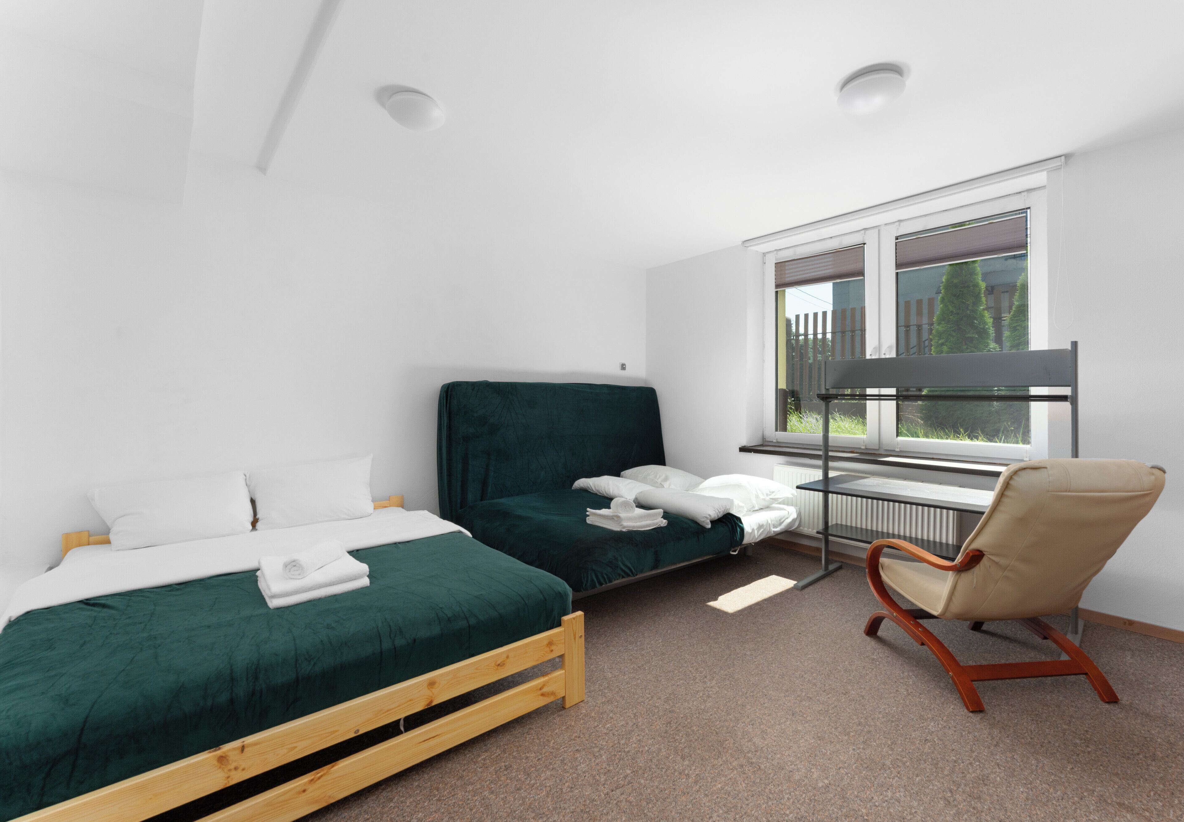 Ein Schlafzimmer mit zwei Betten, einem Sessel, einem Fenster und einer Heizung.