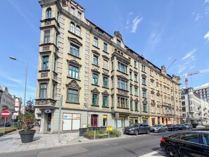 A multi-story building with a classical architectural style, featuring a row of shops on the ground floor and a street view with parked cars. - Słowackiego Chic Apartment (Katowice)