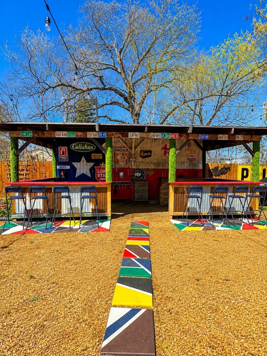 Un área de estar al aire libre con colores vivos, con un camino que lleva a un edificio con varios letreros y logotipos.