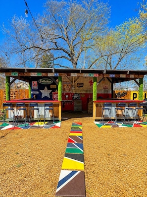 A colorful outdoor seating area with a path leading to a building with various signs and logos. - The Backyard Cantina Walk to Fair Park (Dallas)