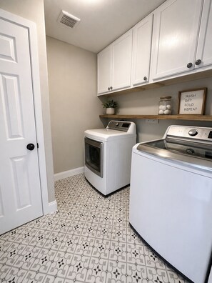 A laundry room with a washing machine and dryer, a potted plant, and a shelf with a framed sign. - The Backyard Cantina Walk to Fair Park (Dallas)