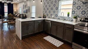 A modern kitchen with dark wood flooring, a central island, dark cabinets, and a backsplash with a floral pattern. - The Backyard Cantina Walk to Fair Park (Dallas)