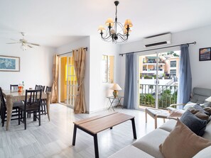 A modern living room with a dining area, a chandelier, and a balcony with a view of the city. - Las Flores de Burriana 5 by Casasol by Interhome (Nerja)