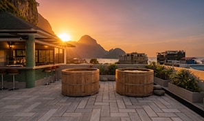 A rooftop terrace with wooden barrels, a bar area, and a view of the sea and mountains at sunset. - Villa V The One and Only, Managed by H Hospitality (El Nido)