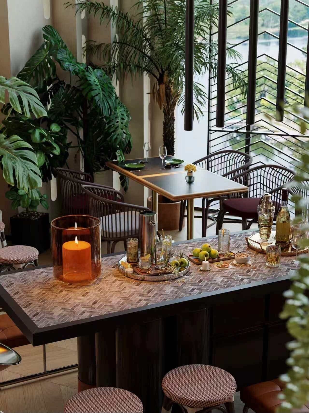 A dining area with a table set for two, surrounded by chairs, with a view of greenery outside.