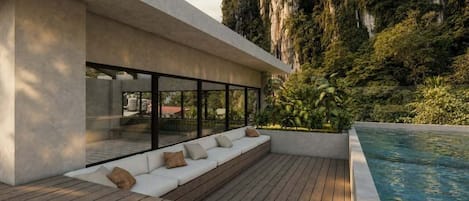Un espace piscine extérieur moderne, doté d’une terrasse en bois, d’un coin salon intégré avec des coussins et offrant une vue sur un paysage montagneux.