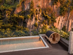 Un área de piscina moderna al aire libre con una sauna de madera y vistas a un acantilado rocoso.