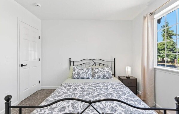 A bedroom with a bed, a nightstand, a window with curtains, and a door.