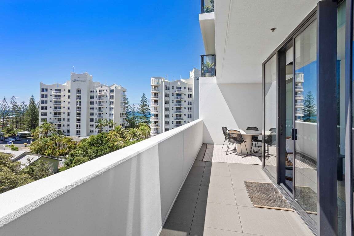 Un balcon avec une table et des chaises, donnant sur un quartier résidentiel composé d’immeubles à plusieurs étages.