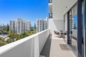 Un balcon avec une table et des chaises, donnant sur un quartier résidentiel composé d’immeubles à plusieurs étages.