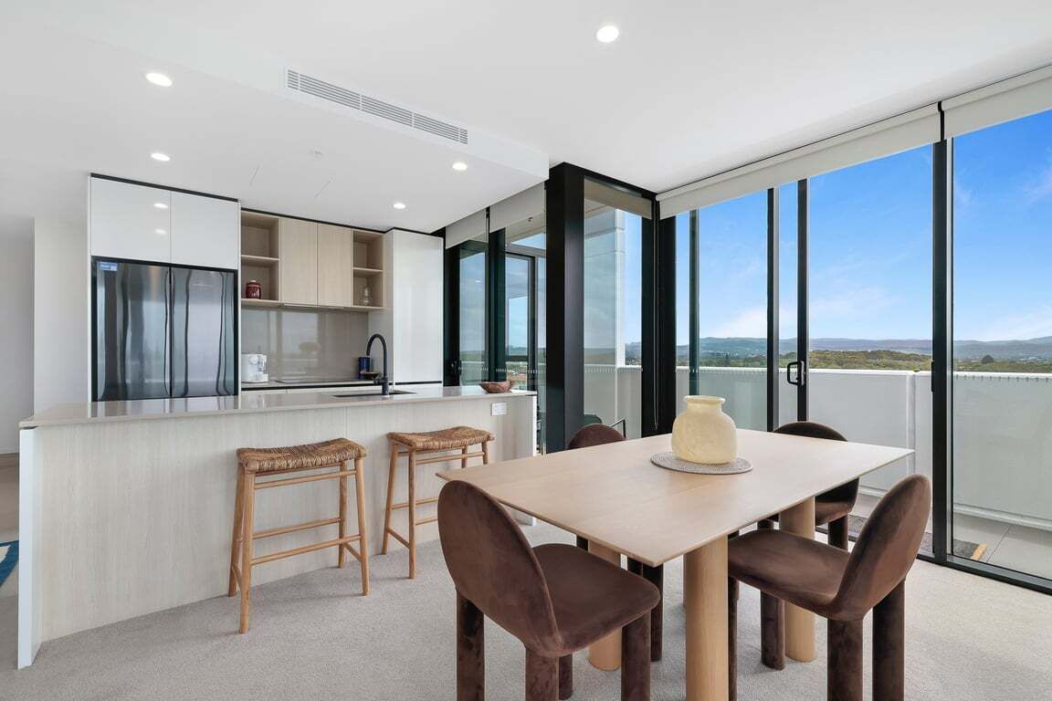 A modern kitchen with a dining area, large windows, and a view of the landscape.