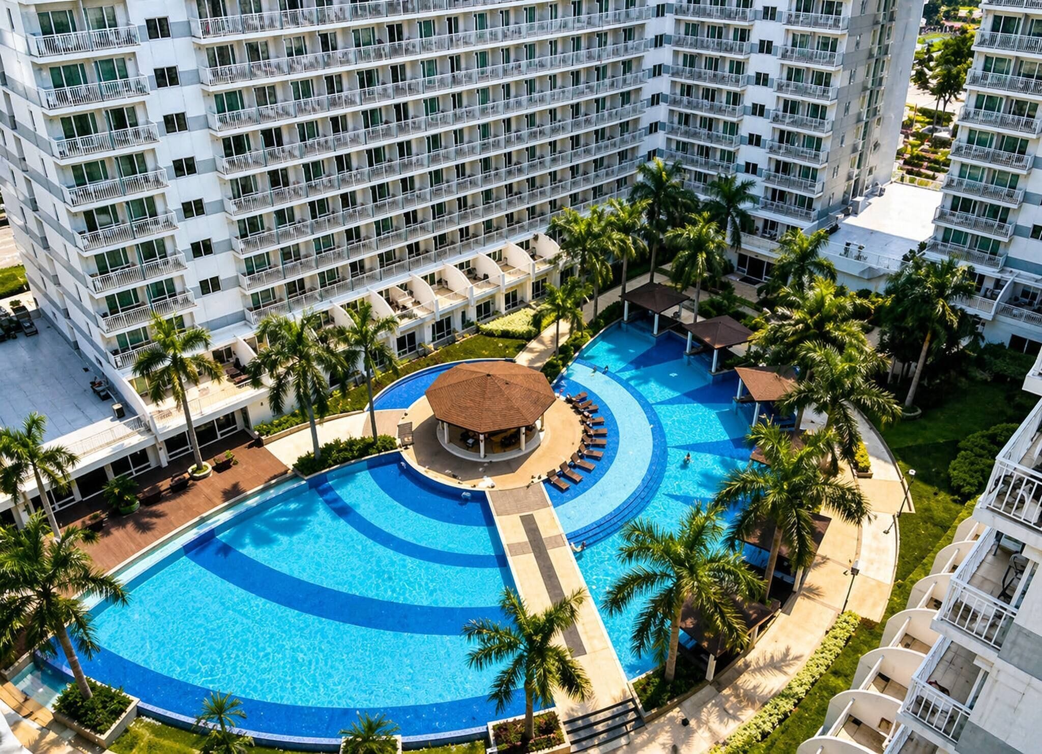 Ein Hotel mit einem großen Schwimmbad, mehreren Balkonen und Palmen.