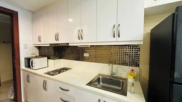 A kitchen with white cabinets, a microwave, a sink, and a black refrigerator.