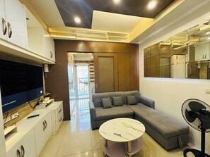 A modern living room with a sectional sofa, a round coffee table, and a flat-screen TV. - Wonderful Urban Retreat Modern Apartment in Pasay Front of Mall of Asia (Pasay)