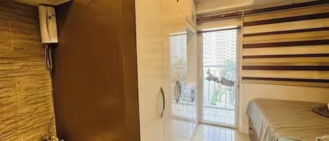 A bedroom with a bed, a wardrobe, a bathroom with a toilet, and a window with a view of buildings.