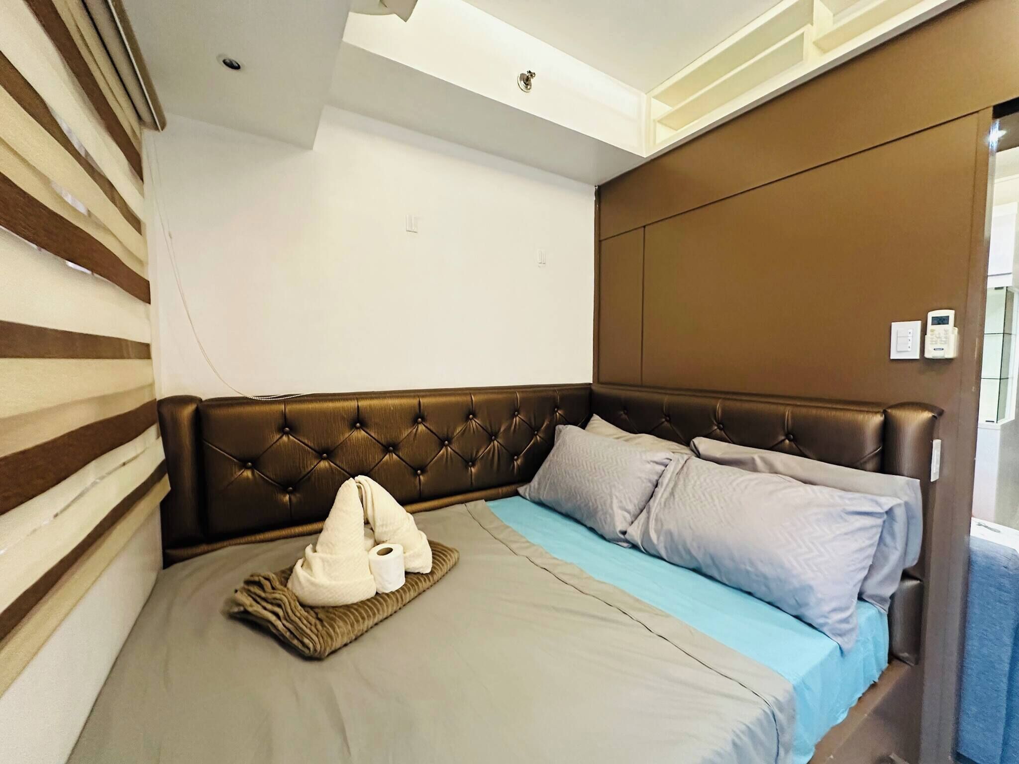 A bedroom with a tufted headboard, a bed with grey and blue bedding, and a bedside table with a lamp.