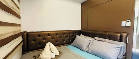 Une chambre à coucher avec une tête de lit capitonnée, un lit avec une literie aux tons de gris et de bleu, et une table de chevet avec une lampe.