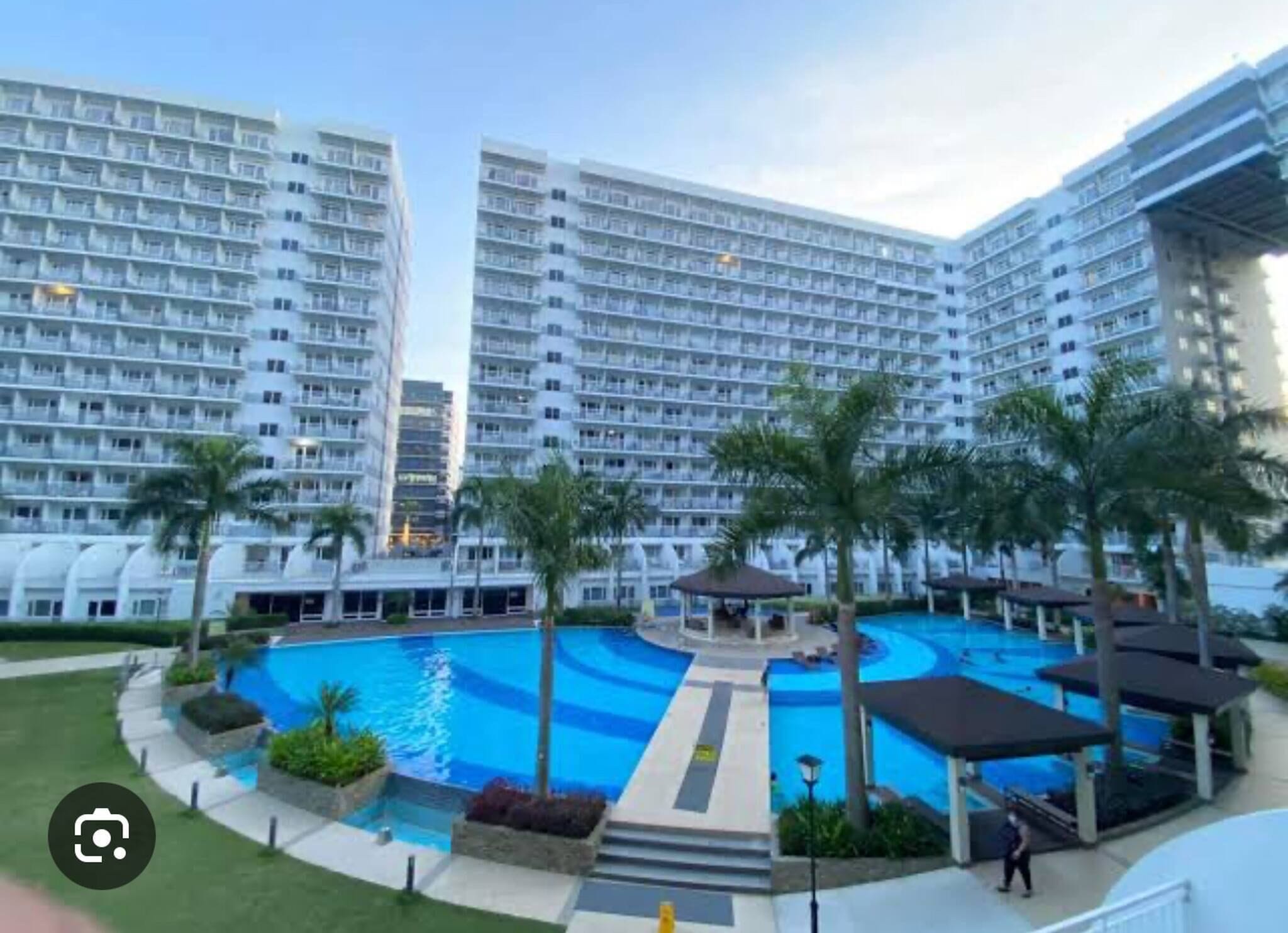 Un hotel moderno con varios edificios altos, una piscina central y palmeras.