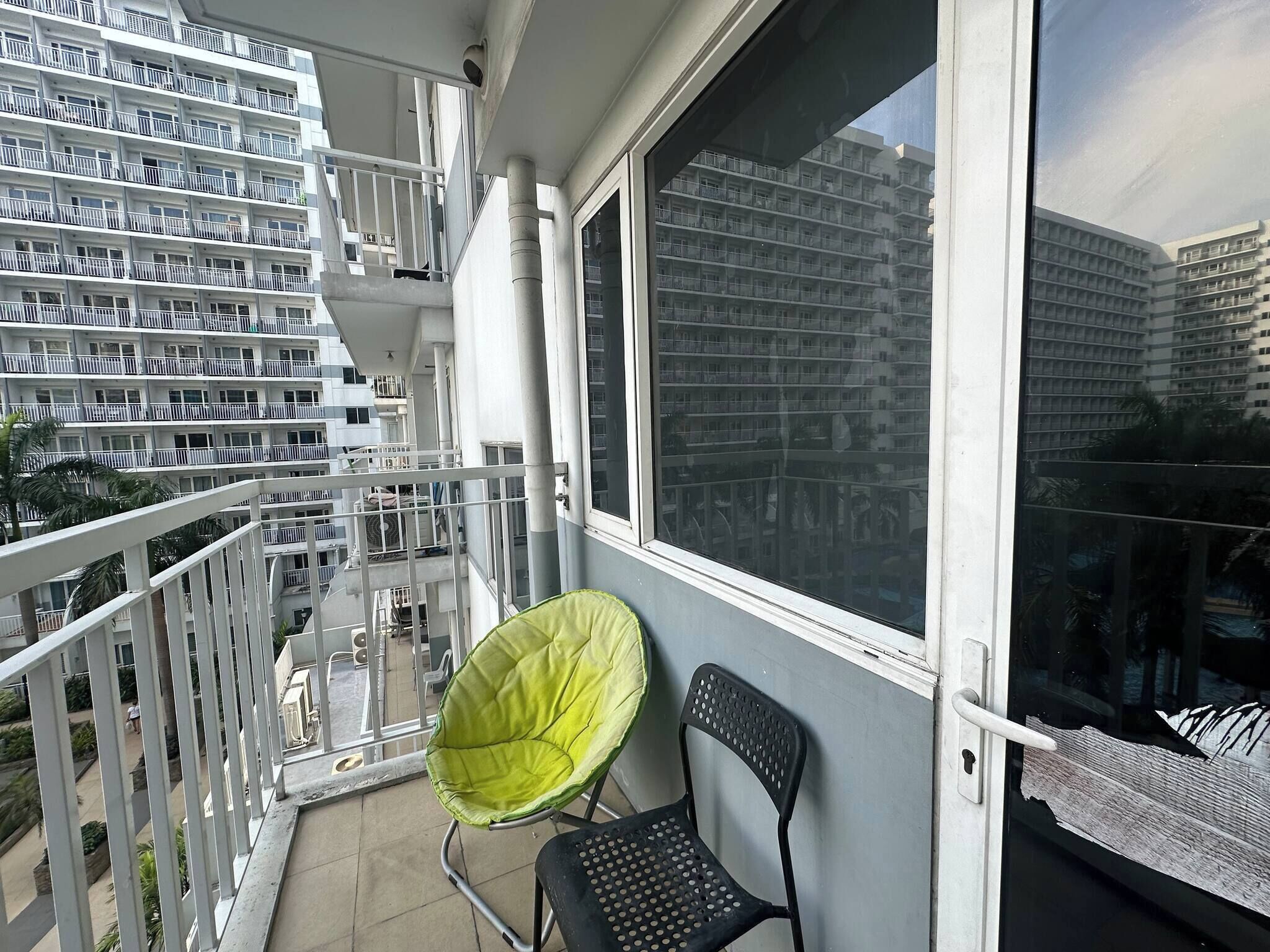 Un balcón con vista a un edificio de gran altura, una silla verde y una silla negra.