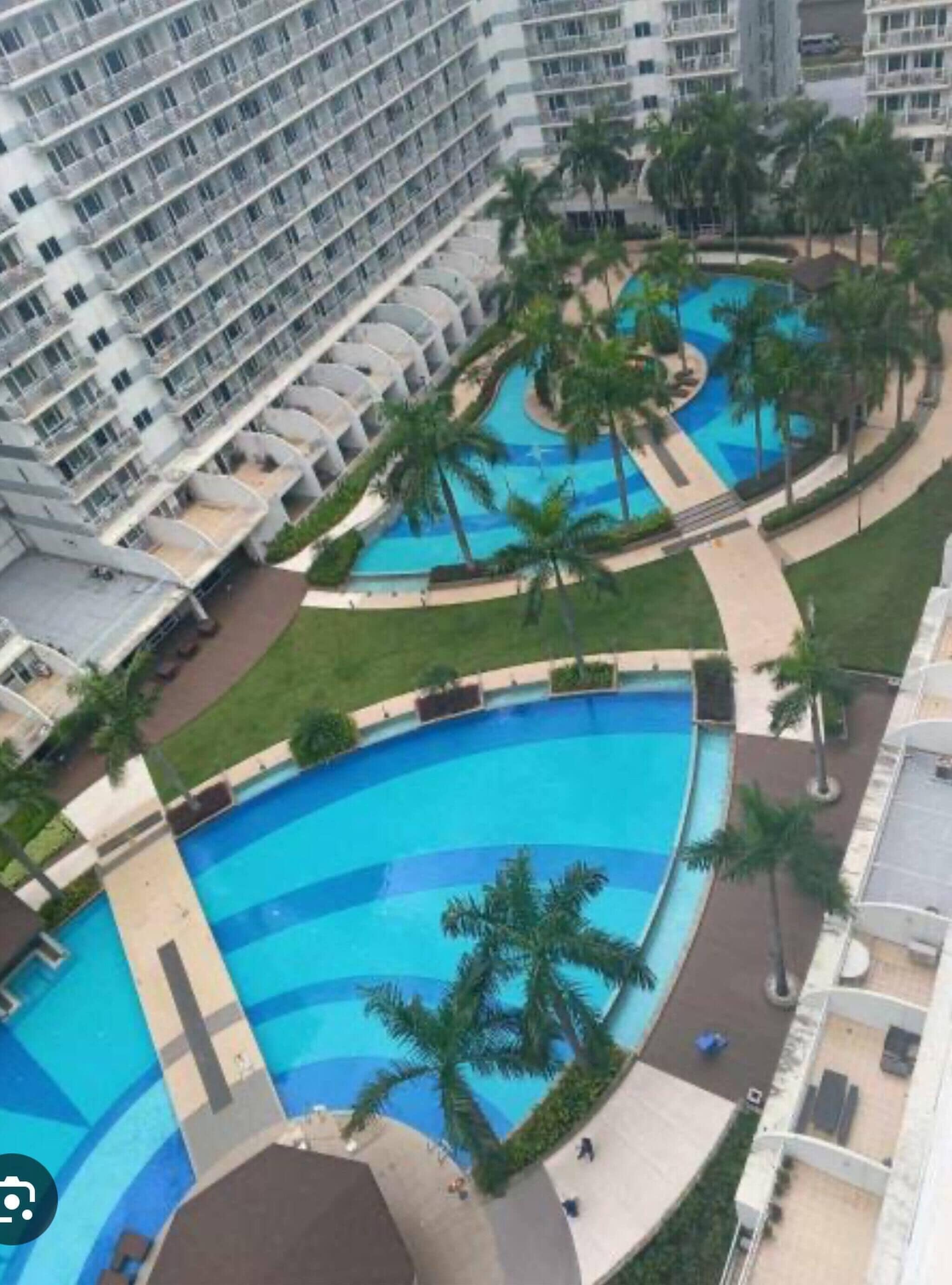 Un hotel moderno de gran altura con múltiples balcones, una piscina central y palmeras alrededor.