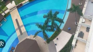 A high-rise hotel with multiple balconies, a central swimming pool, and surrounding palm trees.