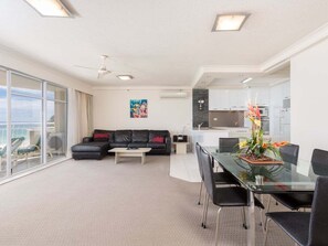 A modern living space with a glass dining table, black leather sofa, and a view through large windows. - 2nd Avenue Apartments - 13B (2B/2B) (Gold Coast)