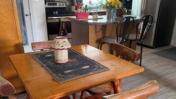 Una mesa de comedor de madera con sillas, una cocina con armarios de madera, un refrigerador y una ventana con cortinas.