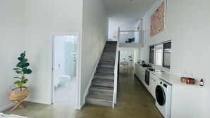 Eine moderne Küche mit Waschmaschine, einer Treppe zum Obergeschoss und einer Pflanze im Vordergrund.
