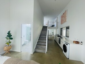 A modern kitchen with a washing machine, a staircase leading to a second floor, and a plant in the foreground. - Peaceful country escape at Twin Tallows Guest House (Cowaramup)