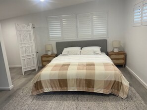 A bedroom with a bed, two bedside tables with lamps, a window with blinds, and a decorative white partition. - Peaceful country escape at Twin Tallows Guest House (Cowaramup)
