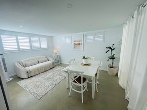 A modern living room with a sofa, dining table, chairs, and a potted plant. - Peaceful country escape at Twin Tallows Guest House (Cowaramup)