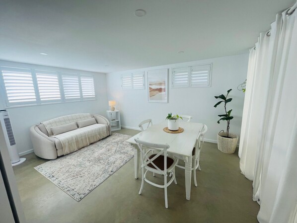 A modern living room with a sofa, dining table, chairs, and a potted plant.