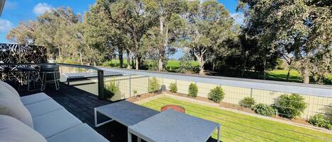 A patio with outdoor seating, a view of a landscaped garden, and a fence.