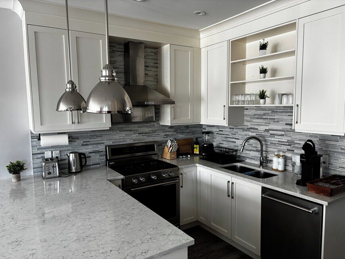 Una cocina moderna con armarios blancos, estufa de acero inoxidable y encimera de mármol.